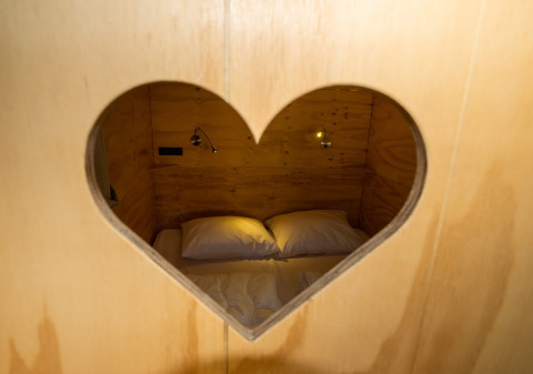Gezicht op een knus bed door een hartvormig raam in Air Lodge 2.0, Papillon Country Resort, Nederland.
