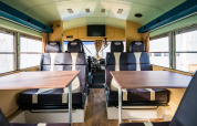 Interior de un autobús escolar retro convertido en lodge con asientos y mesas en Papillon Country Resort.
