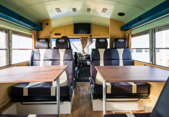 Interior de un autobús escolar retro convertido en lodge con asientos y mesas en Papillon Country Resort.