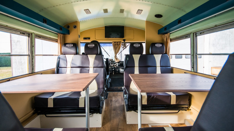 Interior de un autobús escolar retro convertido en lodge con asientos y mesas en Papillon Country Resort.