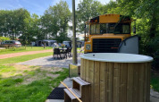Outdoor seating, hot tub, and a retro school bus lodge at Schoolbus Papillon, Papillon Country Resort, Netherlands.