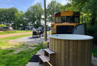 Udendørs scene ved Schoolbus Papillon, Papillon Country Resort, med skolebus, spisebord og vildmarksbad.
