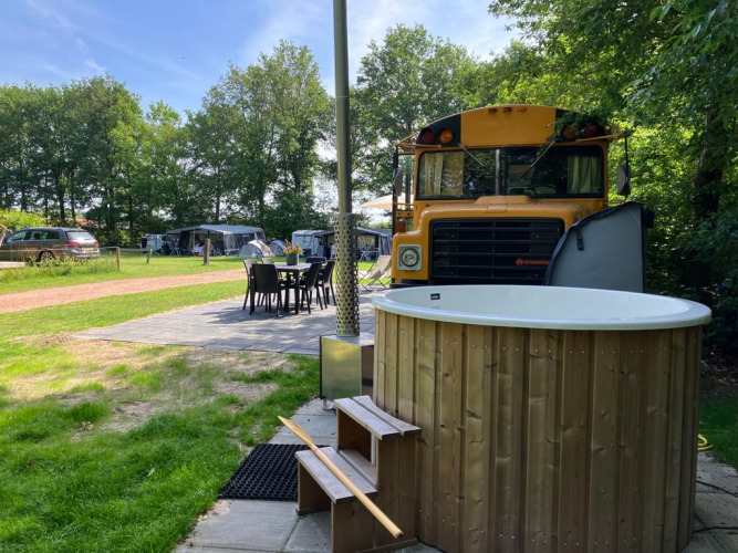 Outdoor seating, hot tub, and a retro school bus lodge at Schoolbus Papillon, Papillon Country Resort, Netherlands.