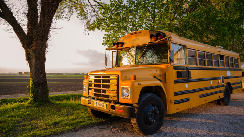 A yellow school bus parked by a tree during sunset at Schoolbus Papillon lodge in a rural setting.