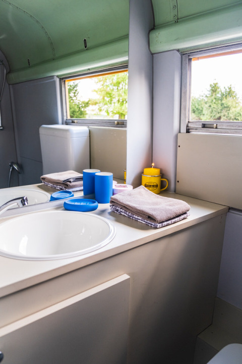 Baño en Schoolbus Papillon del Papillon Country Resort con lavabo, toallas y tazas junto a la ventana.
