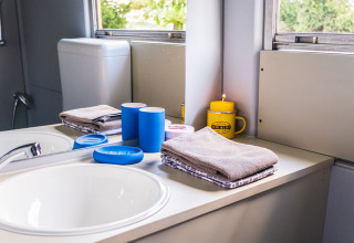 Baño en Schoolbus Papillon del Papillon Country Resort con lavabo, toallas y tazas junto a la ventana.