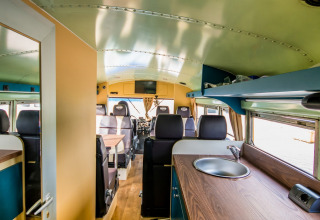 Interno del Schoolbus Papillon lodge al Papillon Country Resort nei Paesi Bassi, con cucina e sedute visibili.