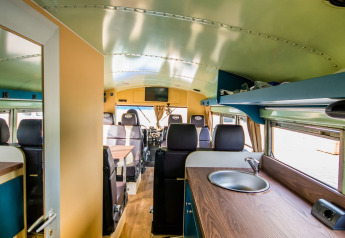 Innenraum der Schoolbus Papillon Lodge im Papillon Country Resort, Niederlande, mit Küche und Sitzecke.