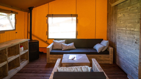 Binnenzicht van de Safarilodge Deluxe bij Papillon Country Resort, met houten meubels en oranje wanden.