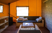Vista interior de la Safarilodge Deluxe en Papillon Country Resort, con muebles de madera y paredes naranjas.