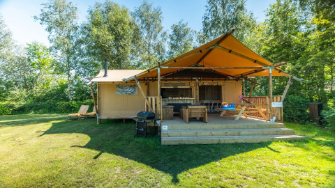 Solrigt billede af Safarilodge Deluxe med overdækket terrasse, grill og grønne omgivelser i naturen.
