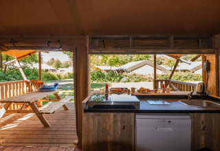 Zicht vanuit de keuken van Safarilodge Deluxe in Papillon Country Resort, met terras en picknickbank buiten.