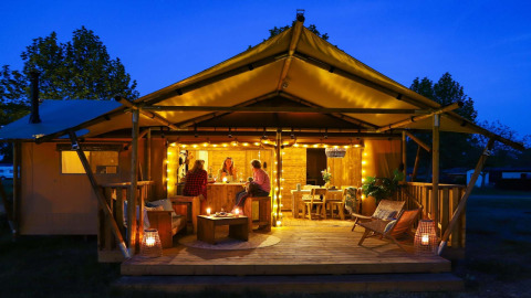 Safarilodge Deluxe en Papillon Country Resort, Países Bajos, iluminada de noche con huéspedes en la terraza.
