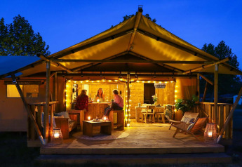 Safarilodge Deluxe en Papillon Country Resort, Países Bajos, iluminada de noche con huéspedes en la terraza.