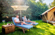 Zwei Personen entspannen auf Liegestühlen unter einem Sonnenschirm vor einem Safarizelt im Papillon Country Resort.