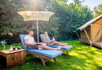 Zwei Personen entspannen auf Liegestühlen unter einem Sonnenschirm vor einem Safarizelt im Papillon Country Resort.