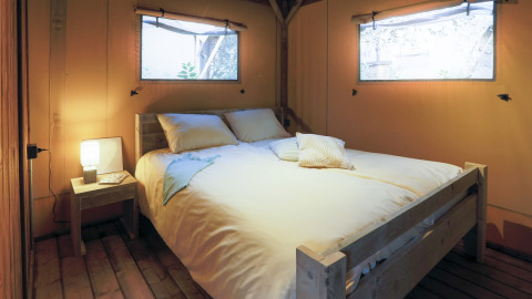 Acogedor dormitorio con cama de madera y ventanas en una tienda glamping rodeada de naturaleza.
