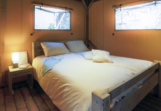 Acogedor dormitorio con cama de madera y ventanas en una tienda glamping rodeada de naturaleza.