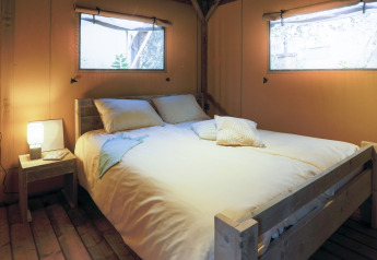 Komfortabelt soveværelse med dobbeltseng og træramme i glamping-indkvartering med naturligt lys.