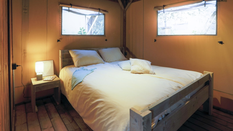 Gemütliches Schlafzimmer mit Doppelbett und Holzmöbeln in einer stilvollen Glamping-Unterkunft.