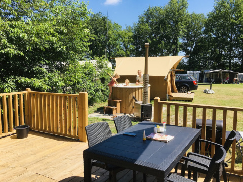 Buiten terras met tafel, stoelen en gezin in hottub bij Airlodge 2.0 Family Hottub op Papillon Country Resort, Nederland.