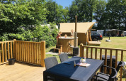 Terraza exterior con mesa, sillas y familia en jacuzzi en Airlodge 2.0 Family Hottub, Papillon Country Resort, Países Bajos.