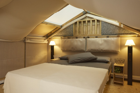 Sfeervolle slaapkamer met bed en lampen in Airlodge 2.0 Family Hottub bij Papillon Country Resort, Nederland, onder tentdak.