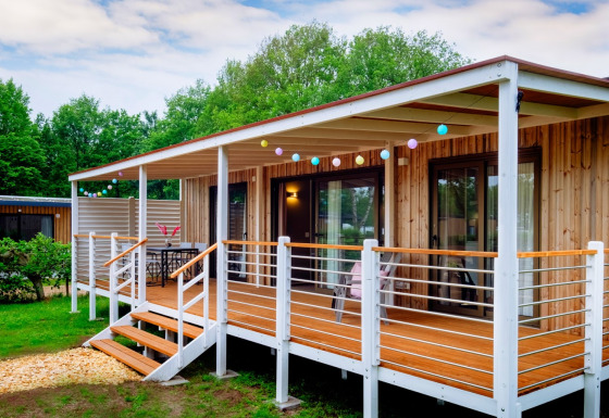 Outdoor view of Cottage Next XL Luxury Superior lodge featuring a wooden deck, string lights, and greenery.