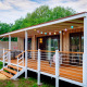 Udendørs billede af Cottage Next XL Luxury Superior lodge med træveranda, lyskæde og grønne omgivelser.
