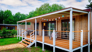 Außenansicht der Cottage Next XL Luxury Superior Lodge mit Holzveranda, Lichterkette und grüner Umgebung.