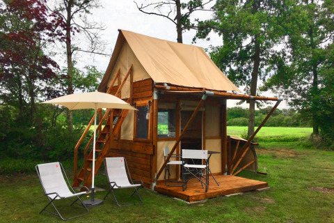 Pequeña casa llamada Airstay con terraza de madera, sillas y sombrilla en un entorno verde y natural.