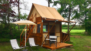 Kleine houten tiny house Airstay met stoelen en parasol op het terras in een groene, landelijke tuin.