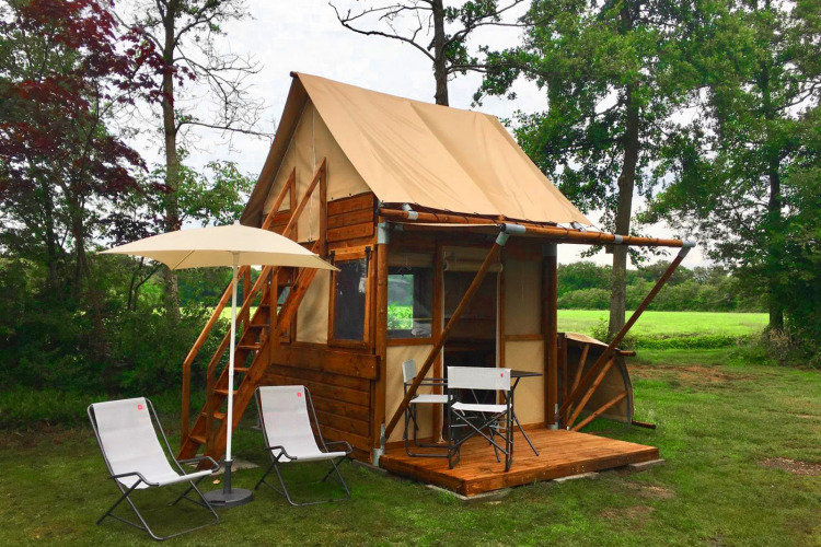 Tiny house called Airstay with wooden siding, small porch, chairs, and umbrella in a lush green yard.