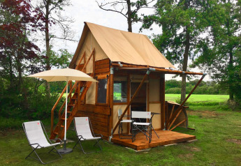 Kleine houten tiny house Airstay met stoelen en parasol op het terras in een groene, landelijke tuin.