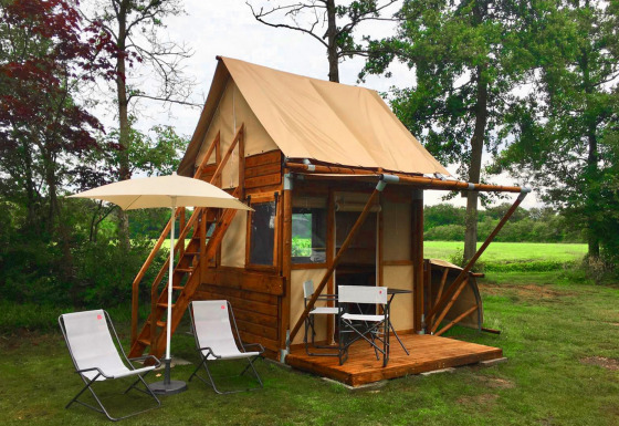 Tiny house called Airstay with wooden siding, small porch, chairs, and umbrella in a lush green yard.