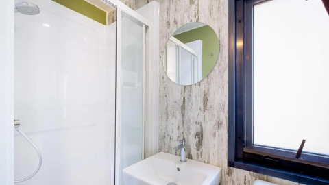 Modernes Badezimmer mit Dusche, rundem Spiegel und Fenster, Cottage Next Midi im Papillon Country Resort, Niederlande.