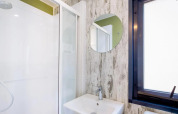 Baño moderno con ducha, espejo redondo y ventana en Cottage Next Midi, Papillon Country Resort, Países Bajos.