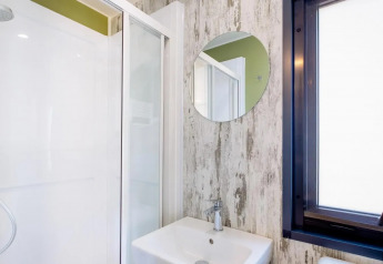 Baño moderno con ducha, espejo redondo y ventana en Cottage Next Midi, Papillon Country Resort, Países Bajos.