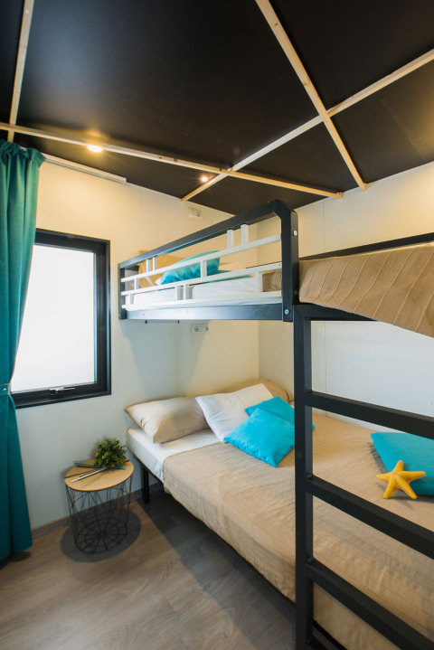 Moderne lodge-værelse med køjeseng, naturligt lys, blå gardiner og puder, på Freed Home i Nederlandene.