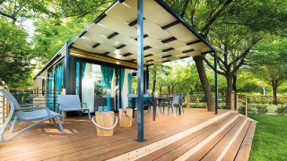 Lodge Freed Home con amplia terraza de madera, mobiliario exterior y cortinas azules entre árboles verdes.