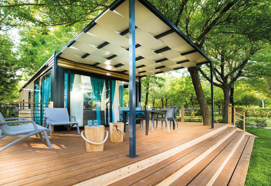 Lodge Freed Home con amplia terraza de madera, mobiliario exterior y cortinas azules entre árboles verdes.