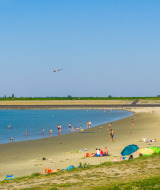 Personas disfrutando en la playa de un parque vacacional con opciones de glamping y clima soleado.