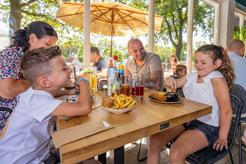 Een gezin geniet van een maaltijd op het terras van Holiday Park BreeBronne, Limburg, Nederland.