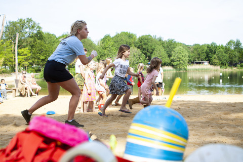 Kinderen spelen enthousiaste strandspellen onder begeleiding aan het meer in vakantiepark BreeBronne, Limburg.
