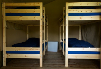 Interno di una tenda safari con quattro letti a castello in legno, biancheria blu e pavimento in legno.