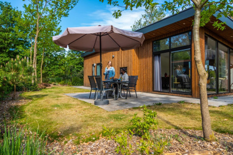 Mensen genieten van een ontspannen moment op het terras van een houten glamping lodge in een vakantiepark.