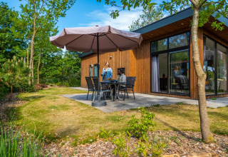 Mensen genieten van een ontspannen moment op het terras van een houten glamping lodge in een vakantiepark.