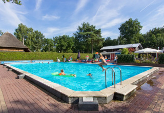 Buitenzwembad bij een vakantiepark met glamping, kinderen spelen en springen in het verfrissende water.