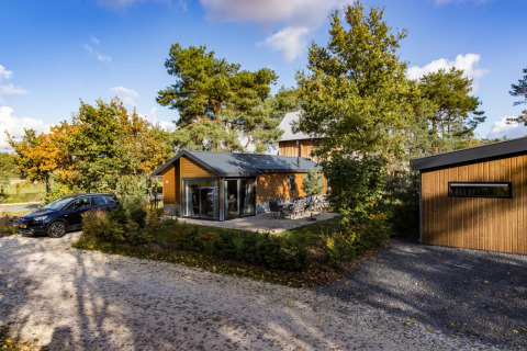 Een modern vakantiehuisje met terras en geparkeerde auto in een bosrijk vakantiepark, ideaal voor glamping.