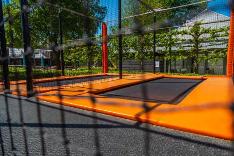 Buiten trampoline in een vakantiepark met glamping, omringd door bomen, hekken en moderne gebouwen.